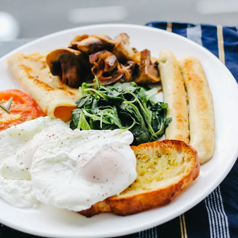 A cooked breakfast: fried eggs, sausages, toast, mushrooms and spinach