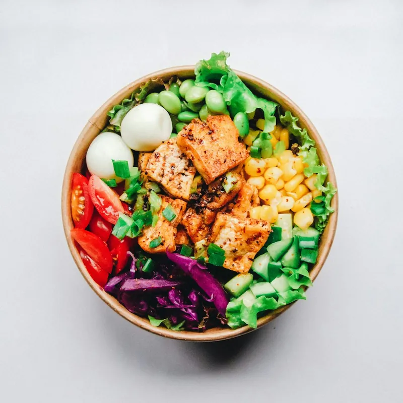 A bowl of grilled chicken, boiled egg, sweetcorn, tomatoes, cucumber and red cabbage